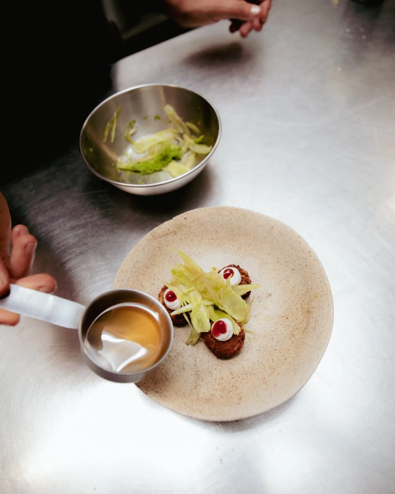 tomato water poured from a measured jug around the falafel at the pass