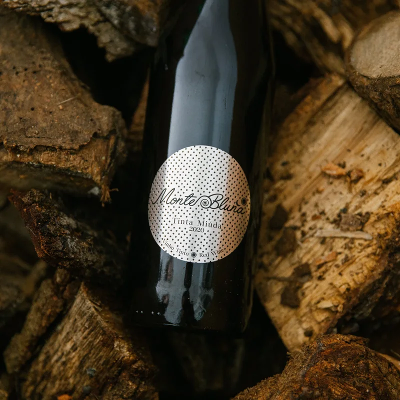a bottle of Monte Bluna Tinta Miúda 2020 among split firewood