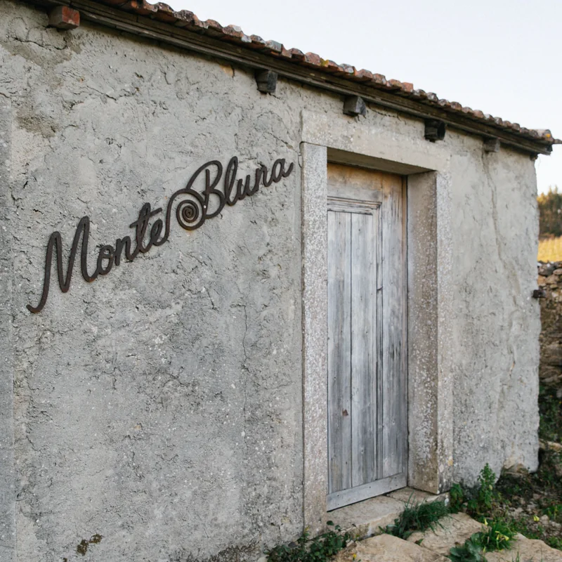 a small stone house with Monte Bluna written in iron on its wall